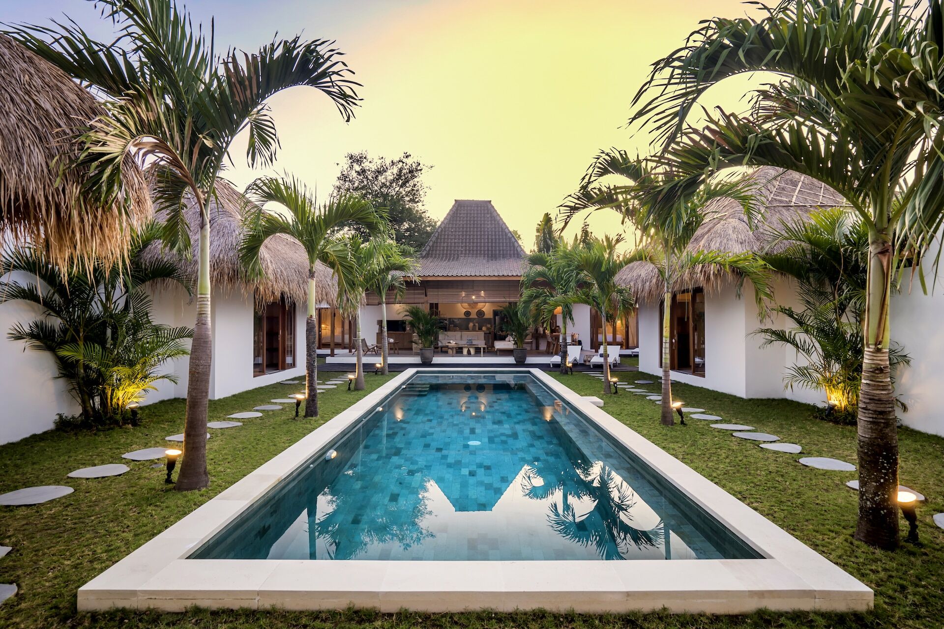 The pool area is surrounded by palm trees and garden at Cocotier Seminyak villa walking distance to Seminyak beach
